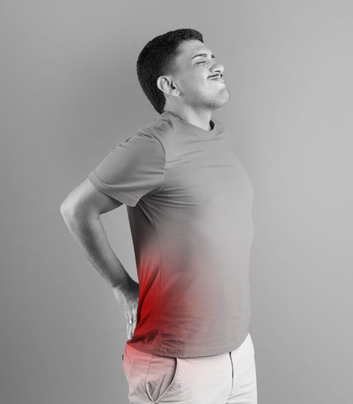 Brazilian man touching aching lower back with red spot on spine, suffering from pain, standing over studio background, black and white photo