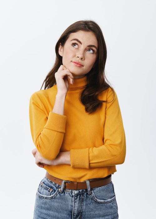 Hmm let me think. Thoughtful young woman planning something, looking at upper left corner and pondering, imaging things on empty space, white background.